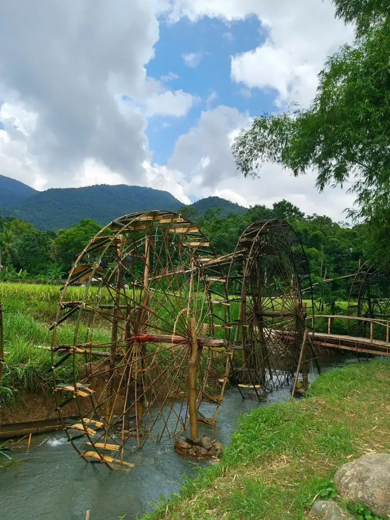 Forest waterfall over rock terraces and wooden water wheels on a canal in Pu Luong